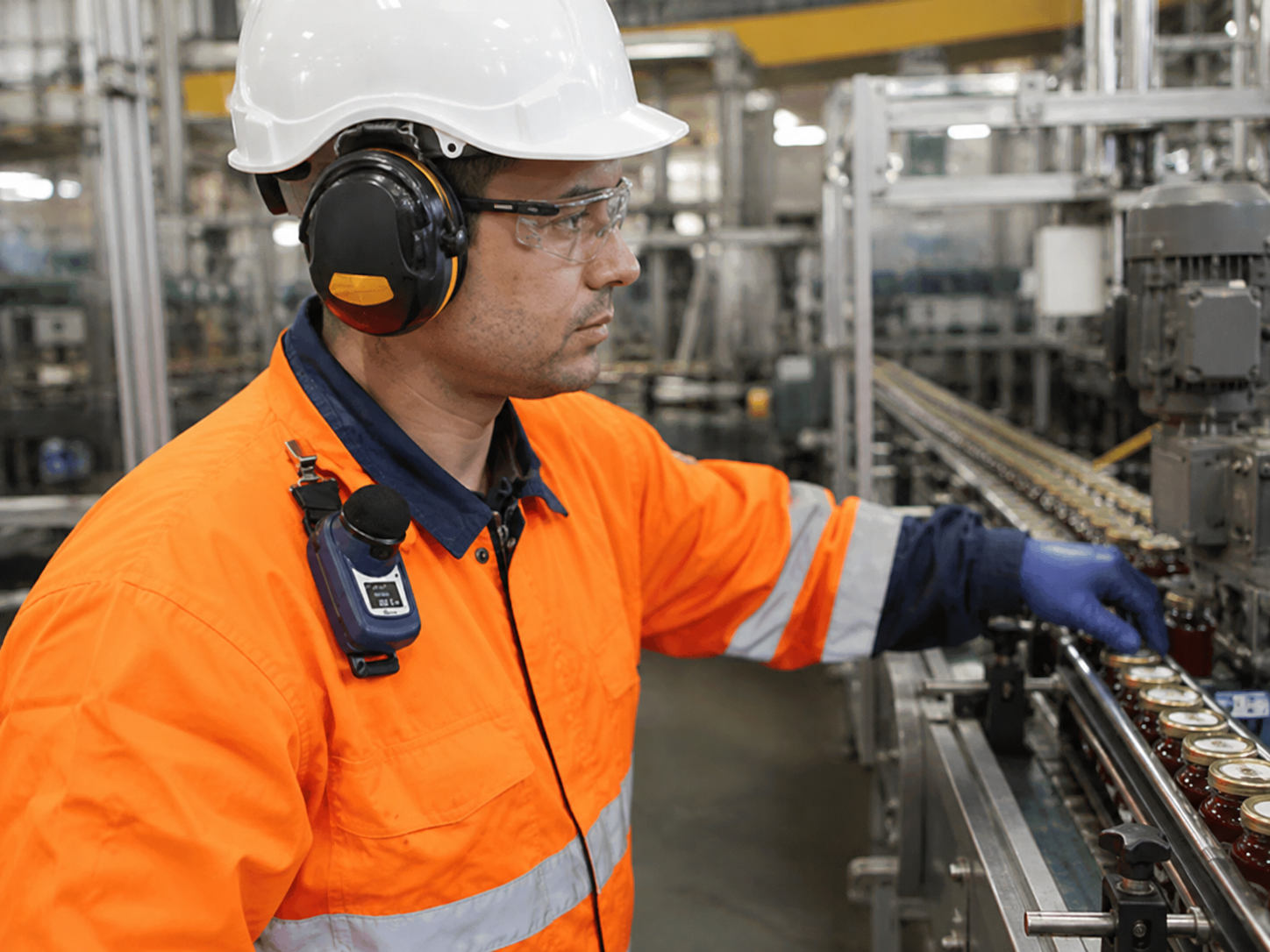 Trabalhador em ambiente industrial utilizando protetor auditivo e dosímetro de ruído